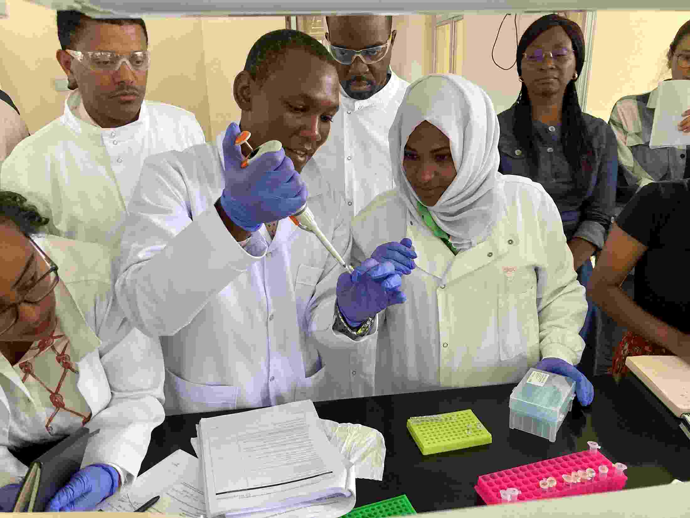Several people wearing protective lab clothing gather round a workbench, using laboratory equipment to test water samples